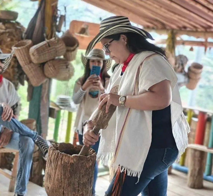 Visitante con vestimenta tradicional de caficultor moliendo en una finca cafetera
