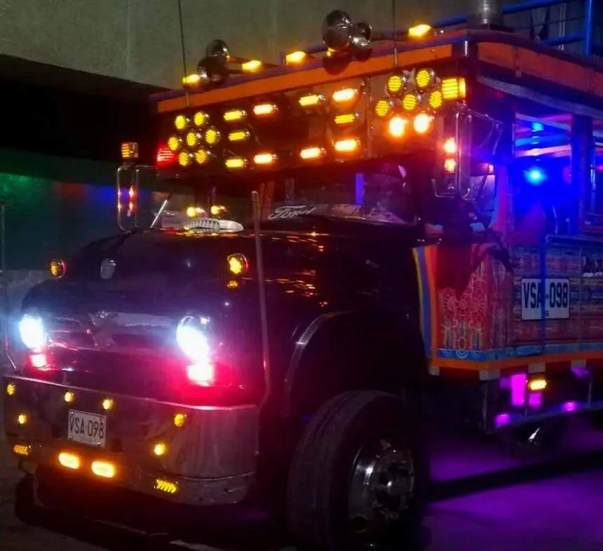 Chiva iluminada con luces naranjas y moradas en la noche