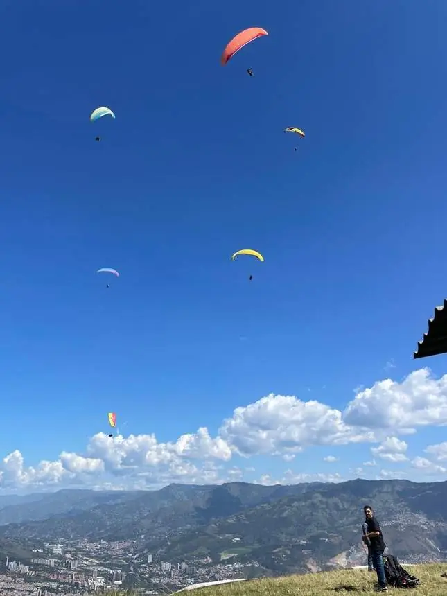 Varios parapentes en un cielo azul sobre las montañas de Medellín